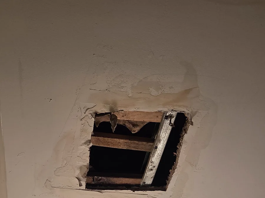 A hole in a ceiling with water-stained, peeling plaster