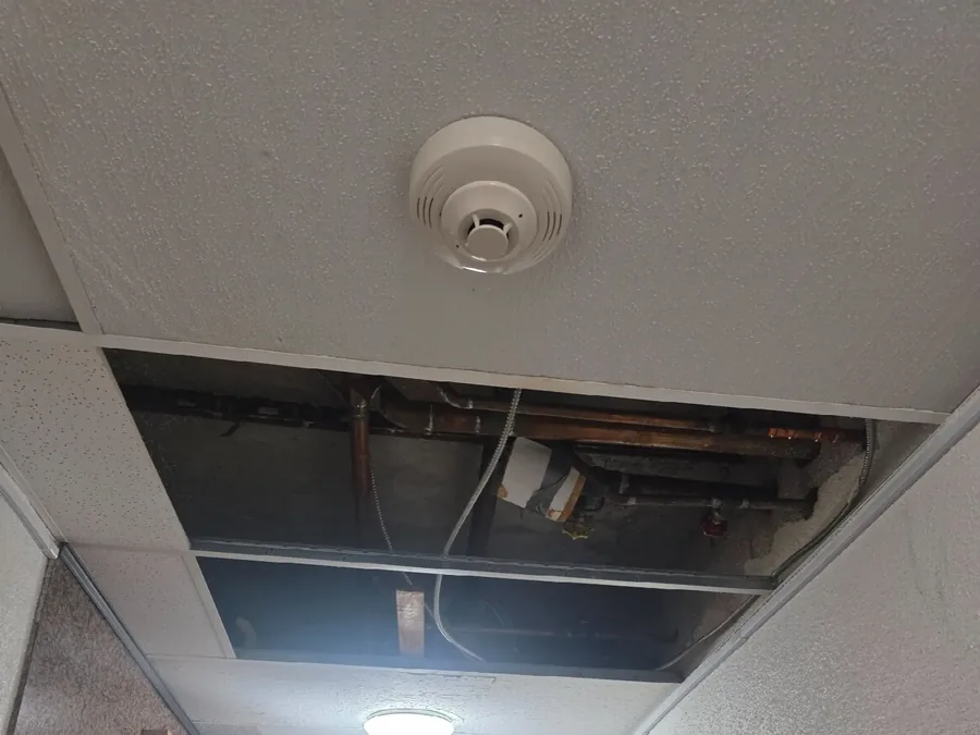 Open ceiling panels and missing tiles in a hallway